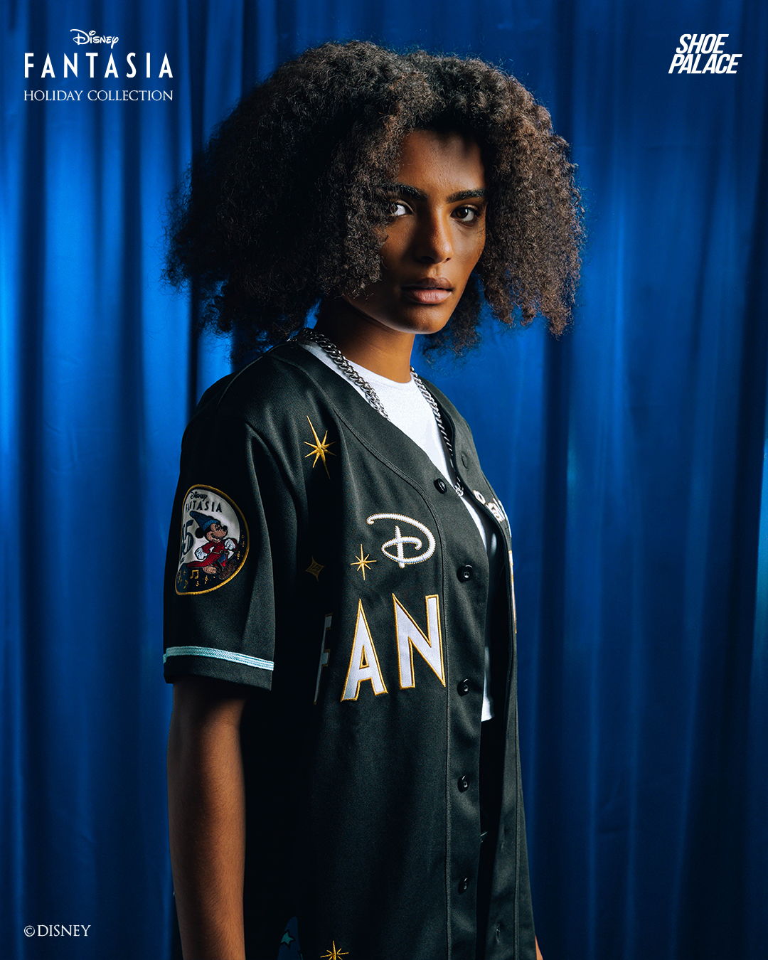 A person with curly hair wearing a black sports jersey against a blue background.