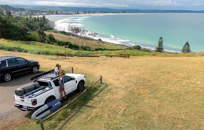 A vehicle with Yakima LockNLoad Platform, awning and surfboards near the beach