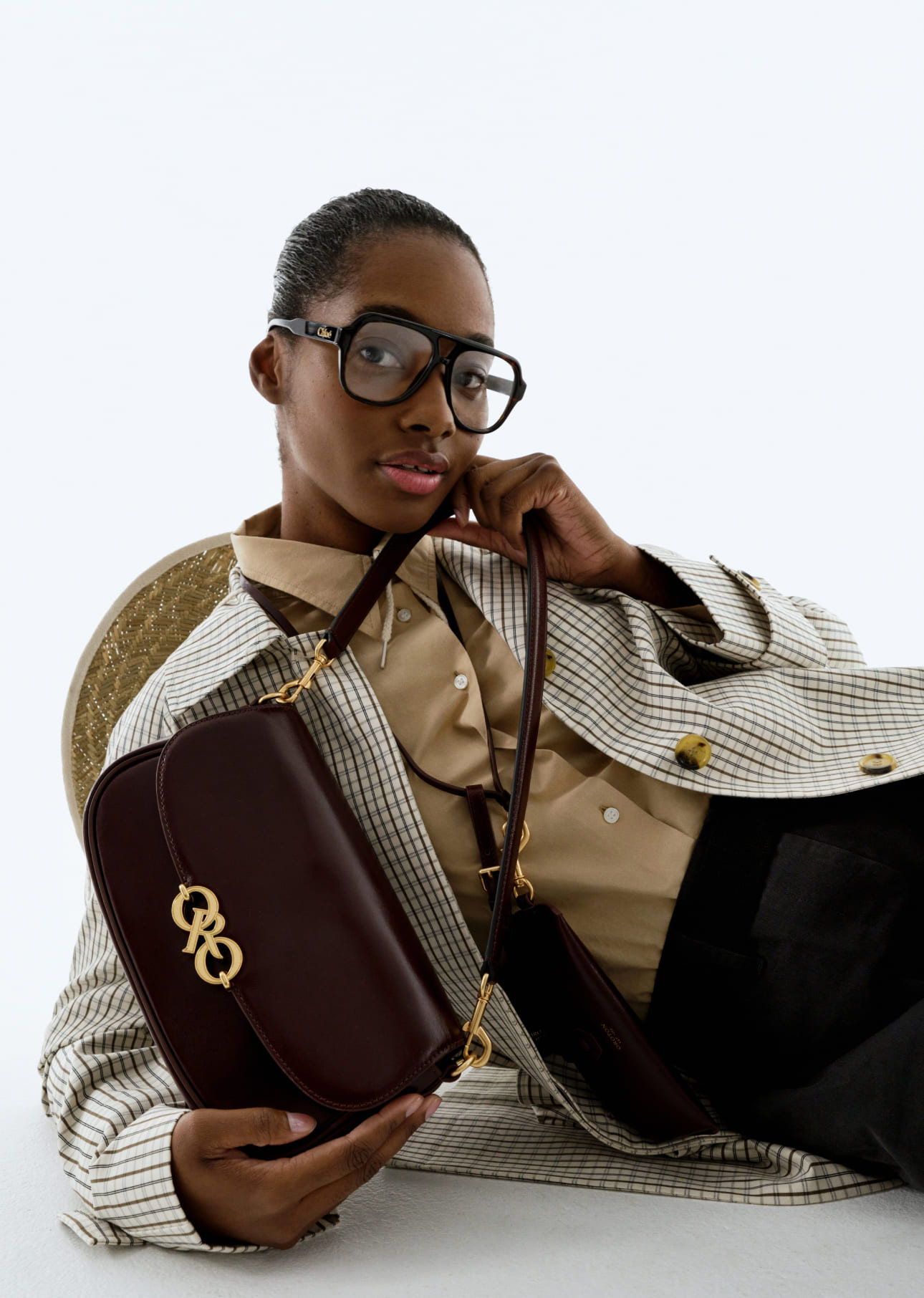 A person wearing glasses holds a brown handbag, dressed in stylish attire.