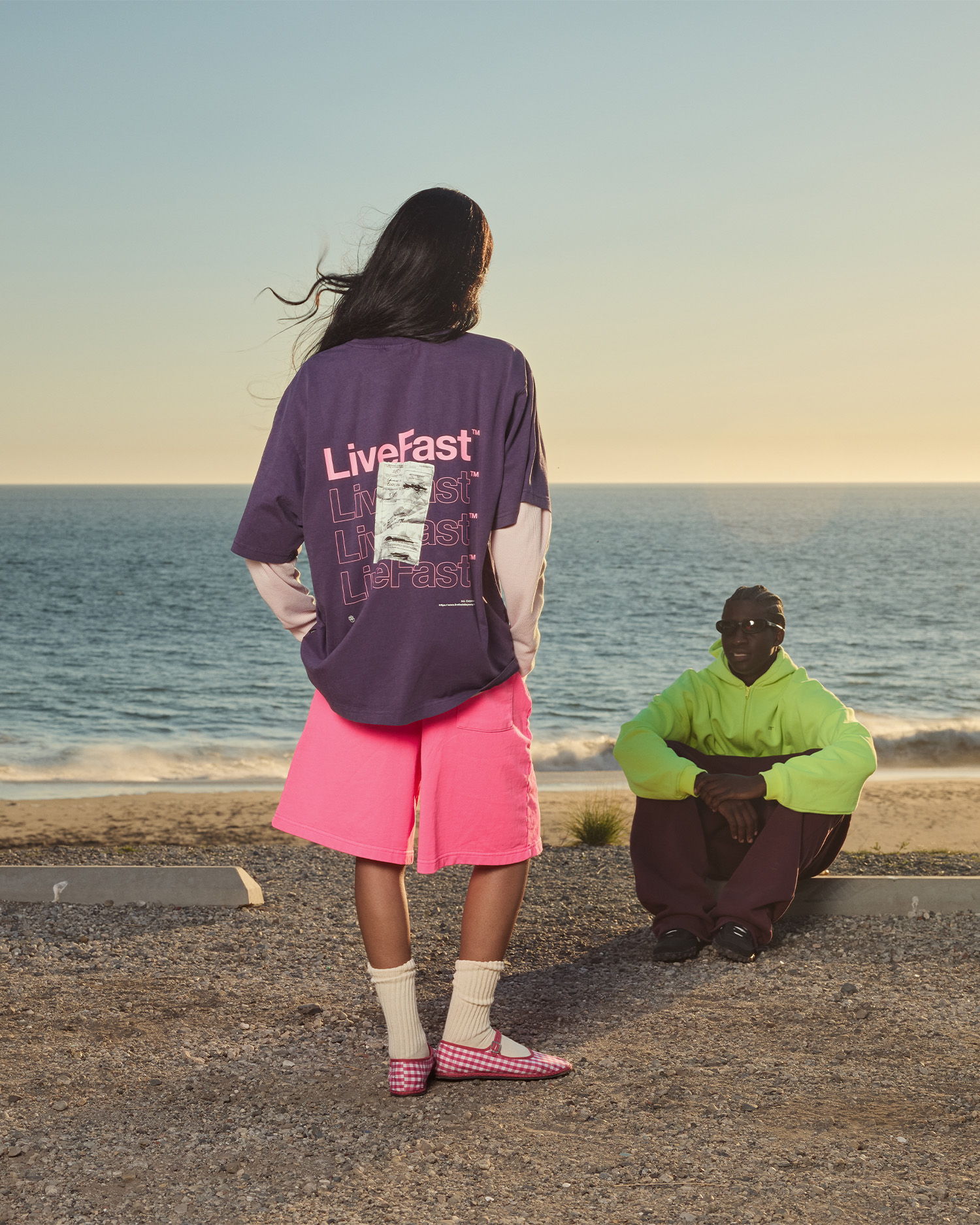 Two people by the sea, one in bright clothing, the other in casual wear.