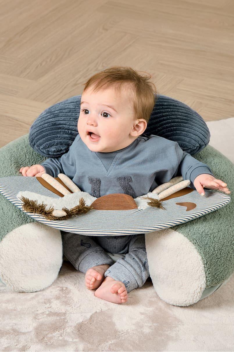 Baby sitting in a soft chair with a playful activity mat.