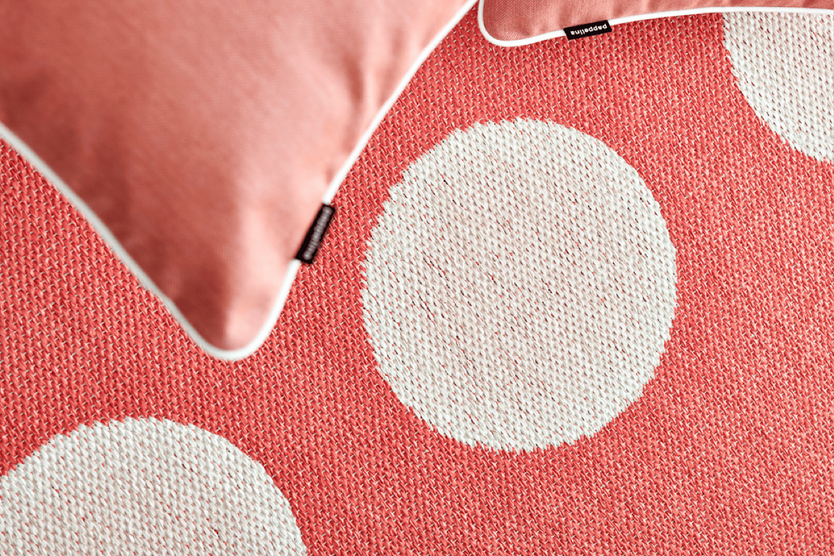 Close-up of a coral and cream flatweave outdoor rug with oversized dot pattern and matching pillow, highlighting the low-profile weave ideal for patios and poolside spaces.
