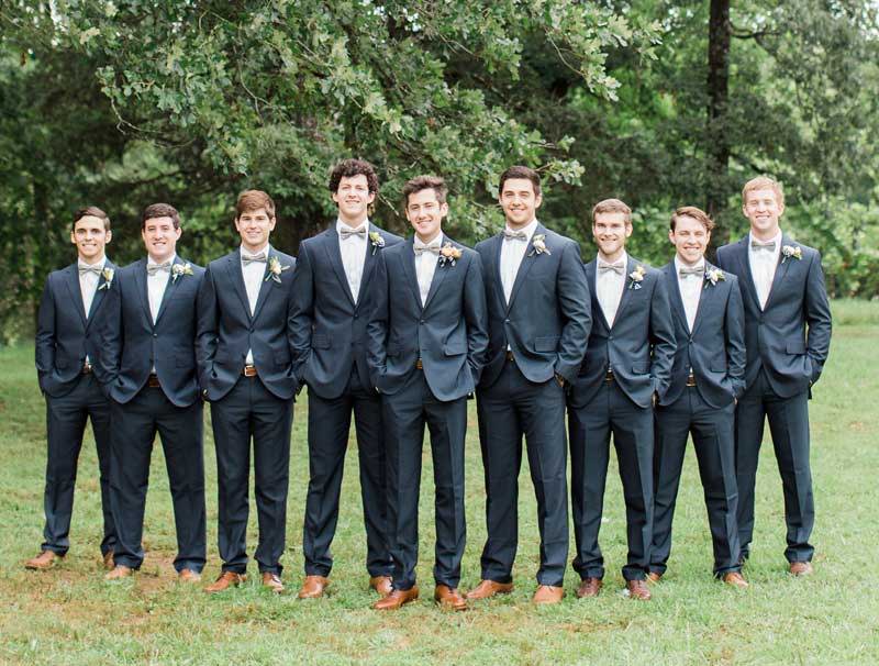 Groomsmen wearing matching mint green bow ties, gray suits and brown oxfords