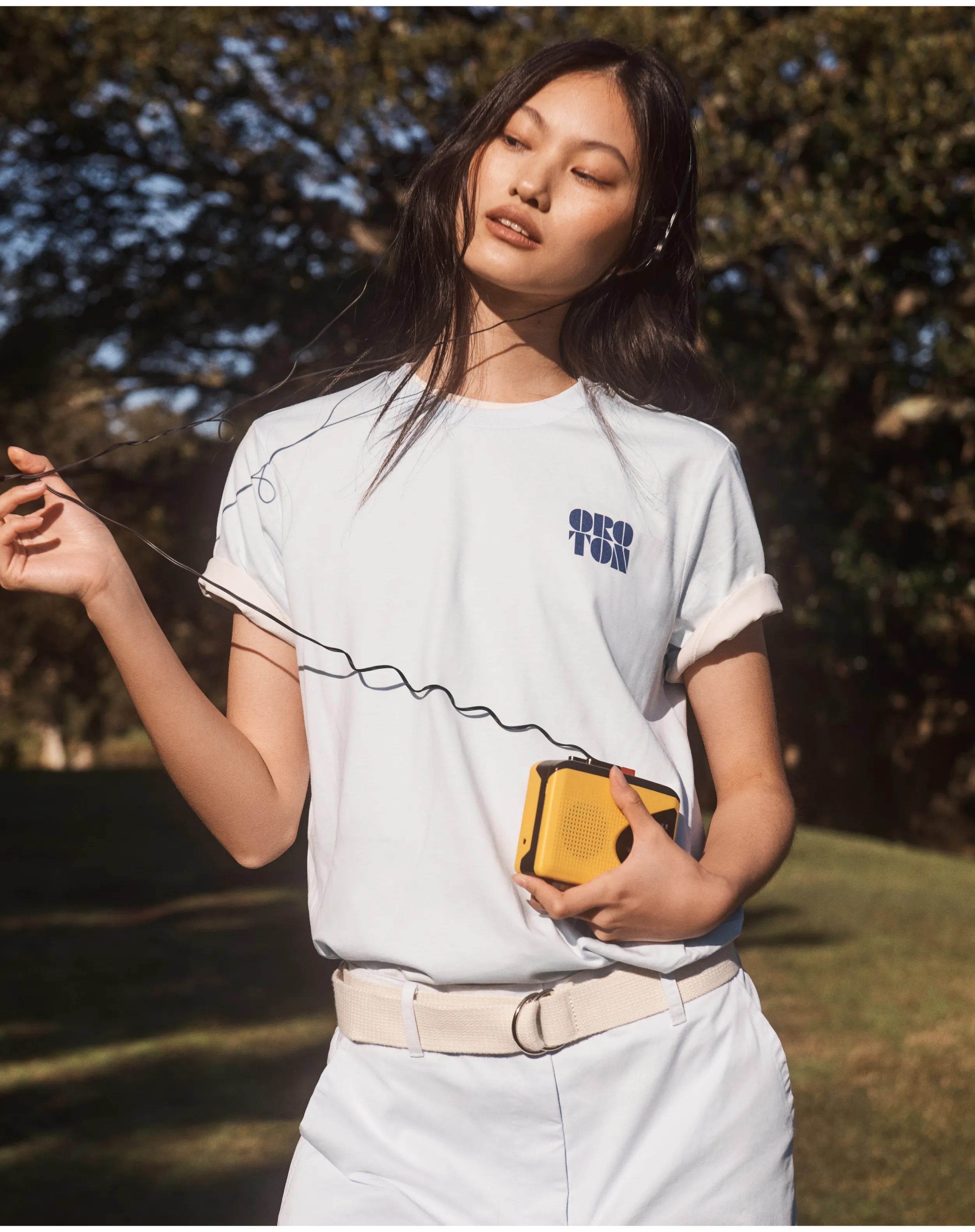Young woman in casual attire, holding a yellow device outdoors.