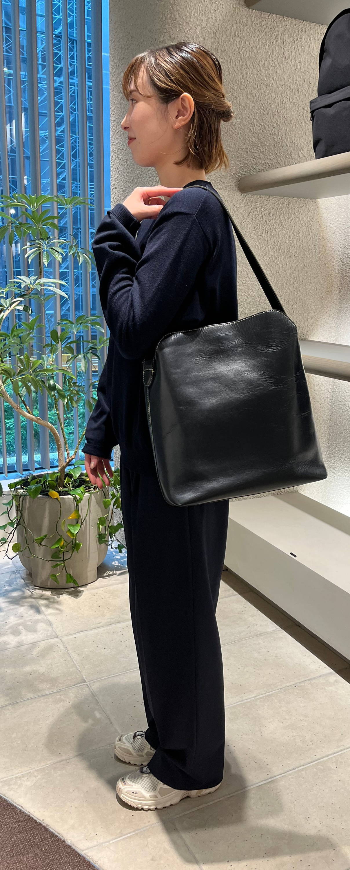 Person wearing a black outfit, holding a black bag in a store setting.