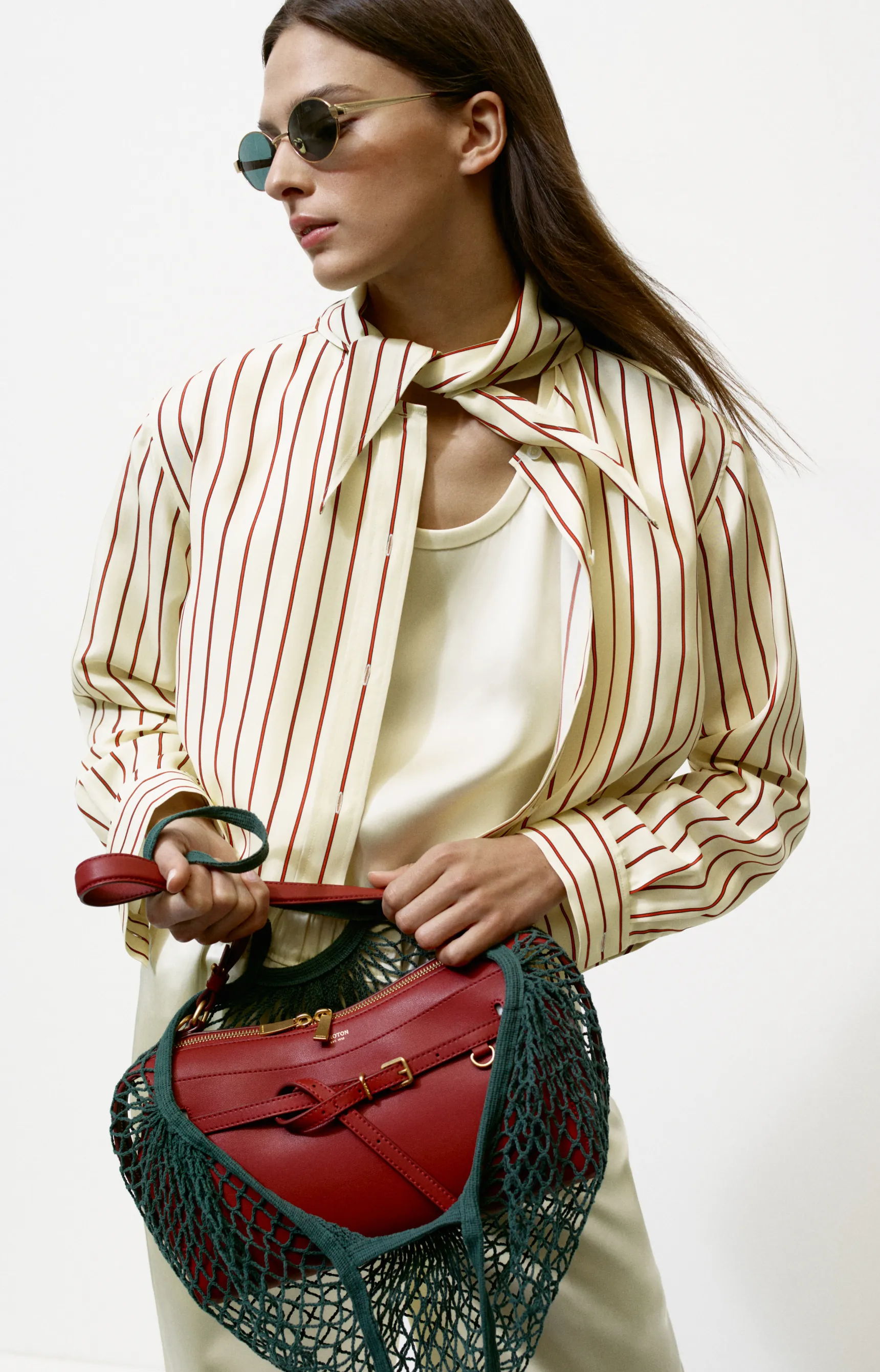 Model wearing a striped shirt, holding a red bag and sunglasses.