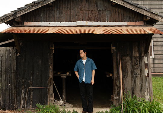 A person standing in front of a rustic wooden barn.