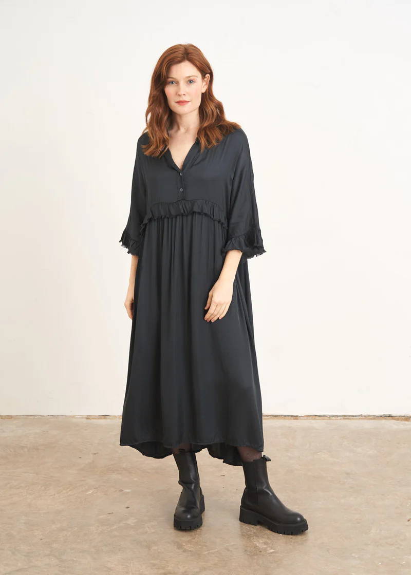 A model wearing a relaxed fitting dark grey satin dress with frill detailing and black chunky chelsea boots