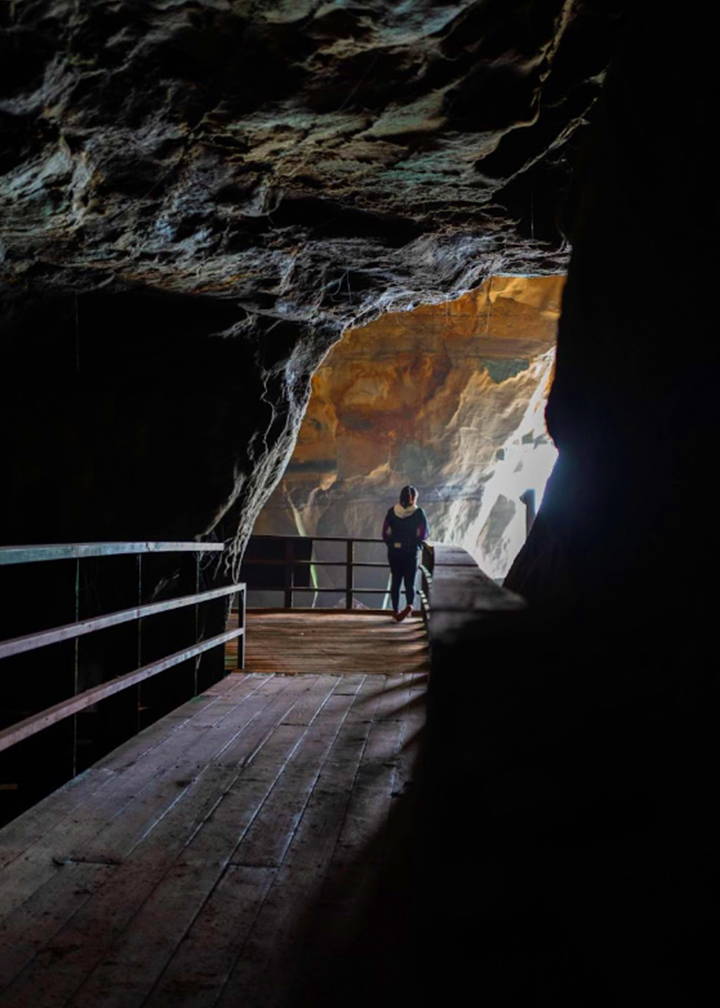 A photo of a woman standing on a wooden bridge inside of a dark sea cave.