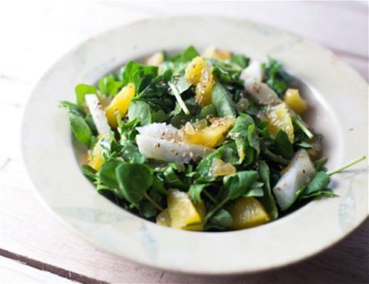 A bowl of mixed green salad with citrus and herbs.