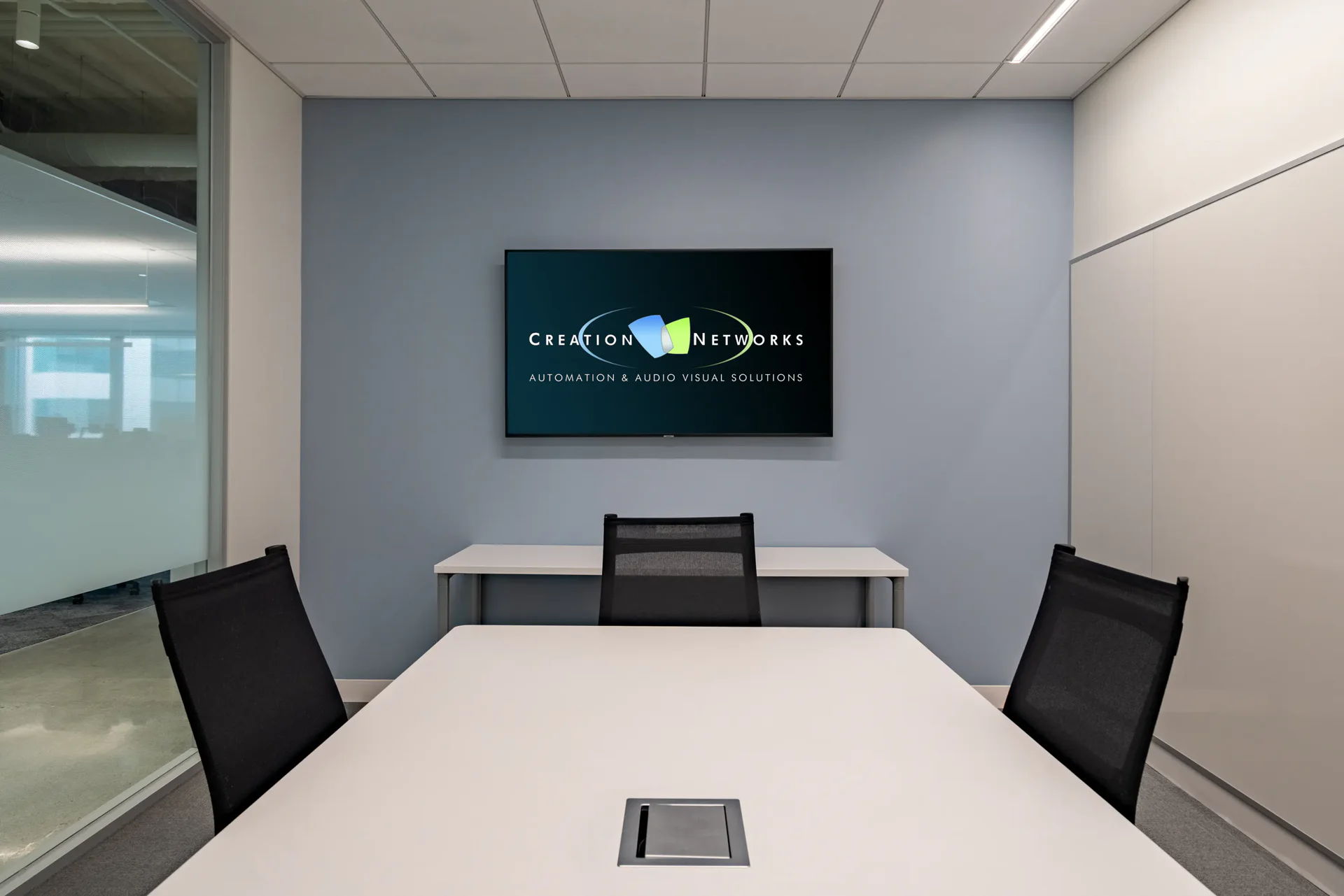 Modern conference room with a table, chairs, and a wall-mounted screen.