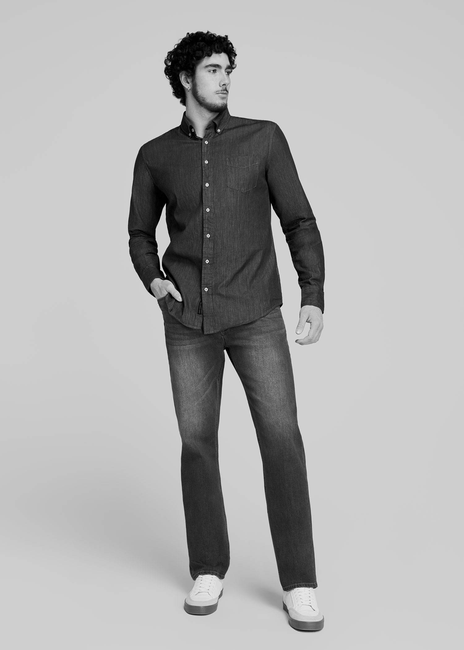 Tall man standing with his hand in his pocket wearing a dark denim shirt and jeans
