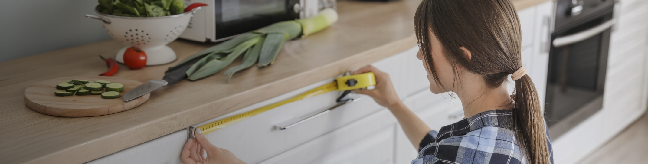 Person measuring a kitchen countertop with a tape measure, surrounded by vegetables.
