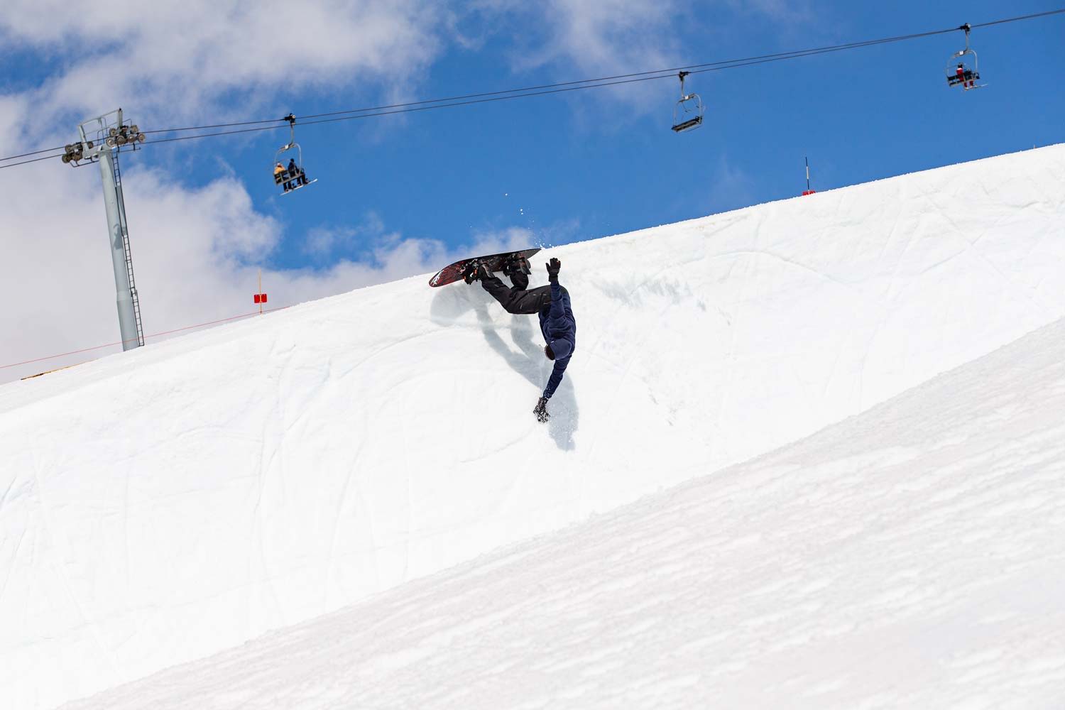 Person snowboarding on a snowy slope under a blue sky with ski lifts.