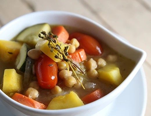 Bowl of vegetable soup with chickpeas, carrots, tomatoes, and herbs.