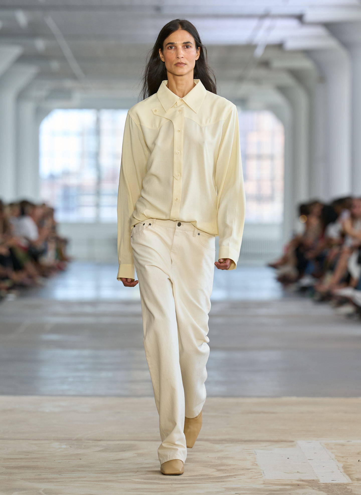 Model walking down the runway in a cream outfit during a fashion show.