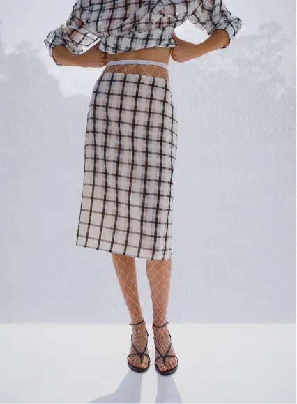 A model poses in a cropped top and plaid skirt.