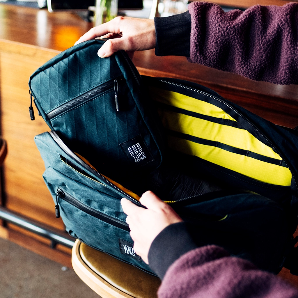 Person holding a backpack with an open inner compartment and a removable pouch.
