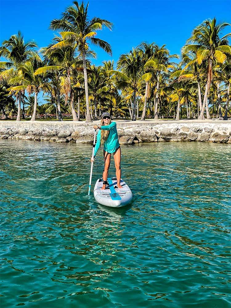 Woman paddling a paddleboard in front of palm trees on a lake