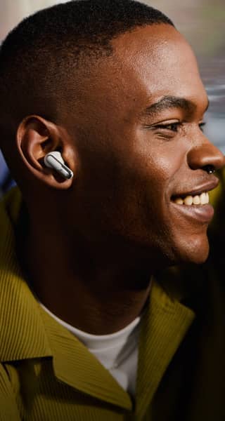 Smiling person wearing earbuds with a blurred background.