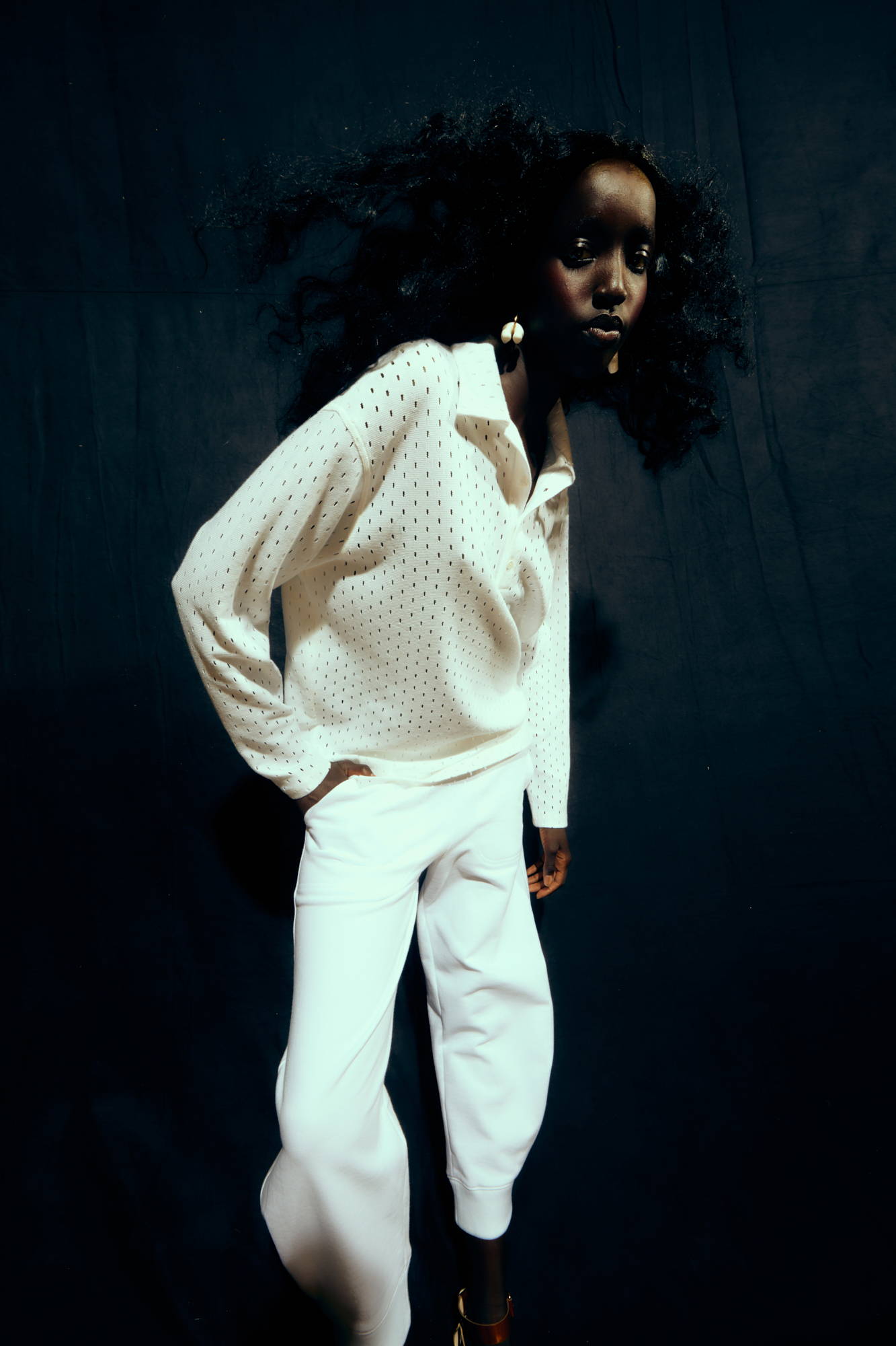 Model in white attire poses against a dark background.