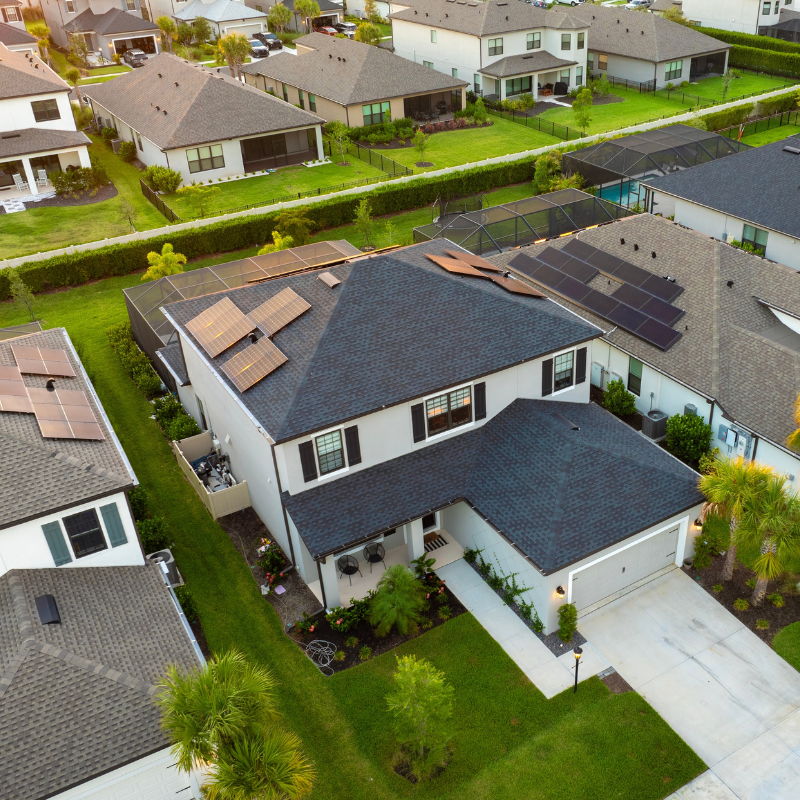 Aerial view of suburban homes with solar panels and a focus on one house.