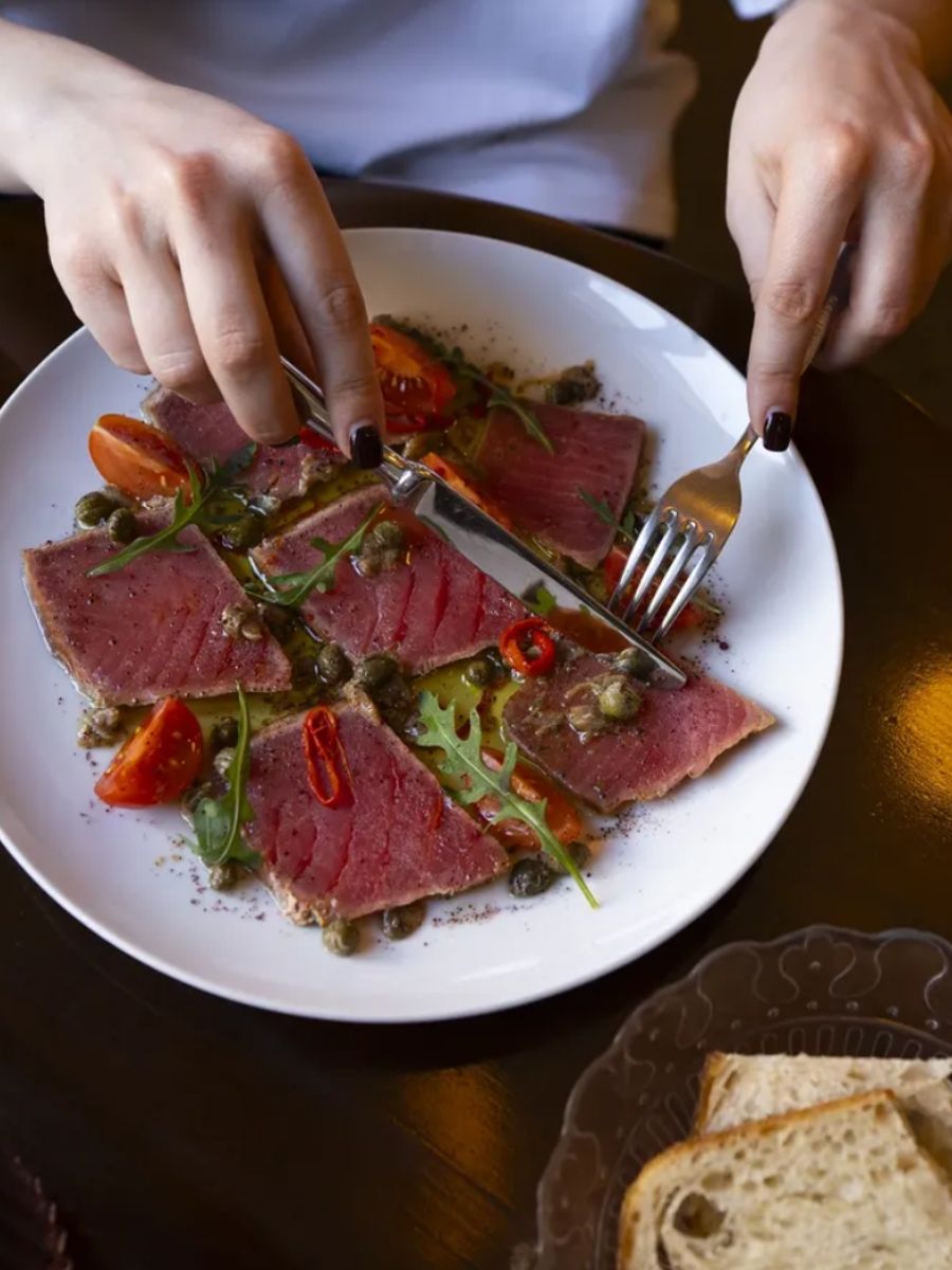 A person cuts into a plate of sliced meat and greens.