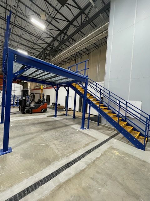 Blue industrial stairs leading to a raised platform in a warehouse.