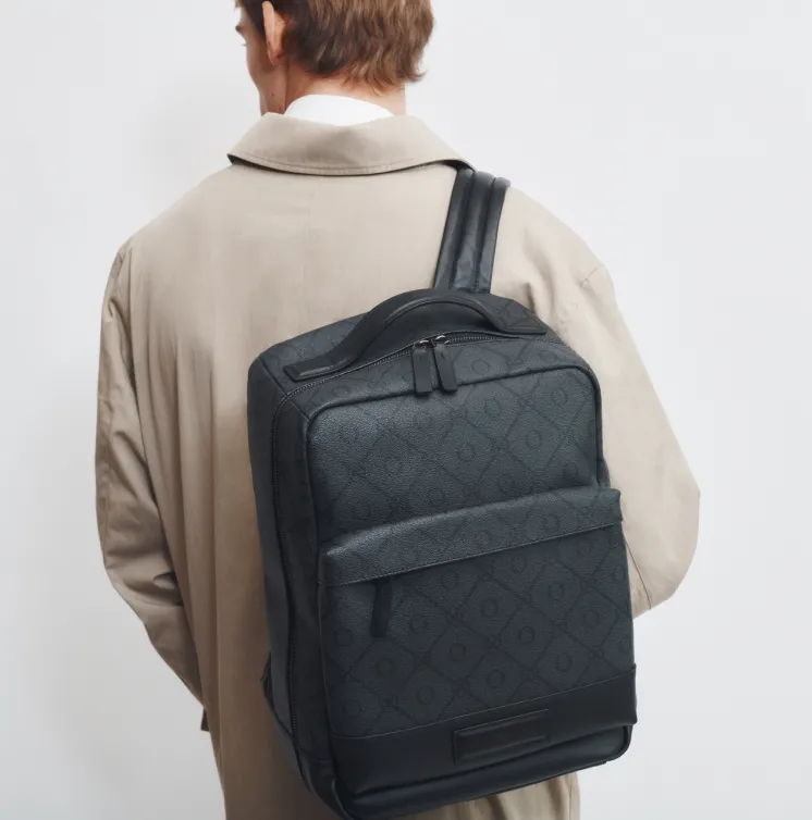 Person wearing a beige coat, carrying a black backpack on their back.