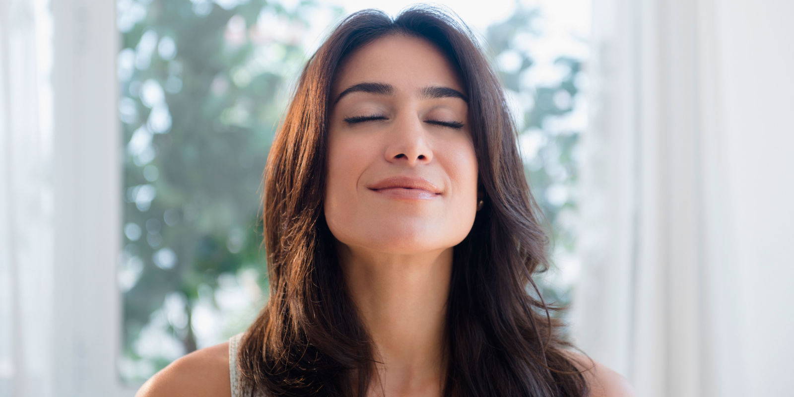 Headshot of woman with eyes closed taking a breath and smiling.