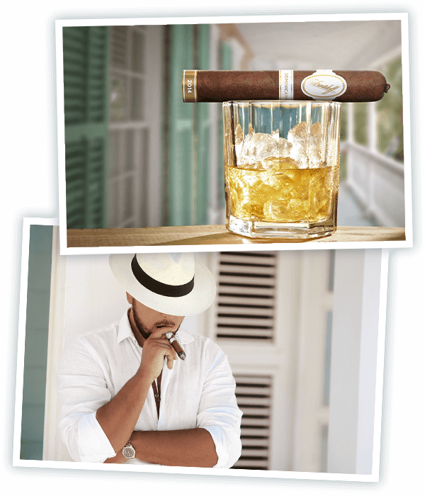 Eine Davidoff Dominicana Robusto Zigarre liegt auf einem Glas Rum auf einer Veranda und ein in Weiß gekleideter Mann mit dominikanischem Hut raucht eine Davidoff Dominicana Zigarre