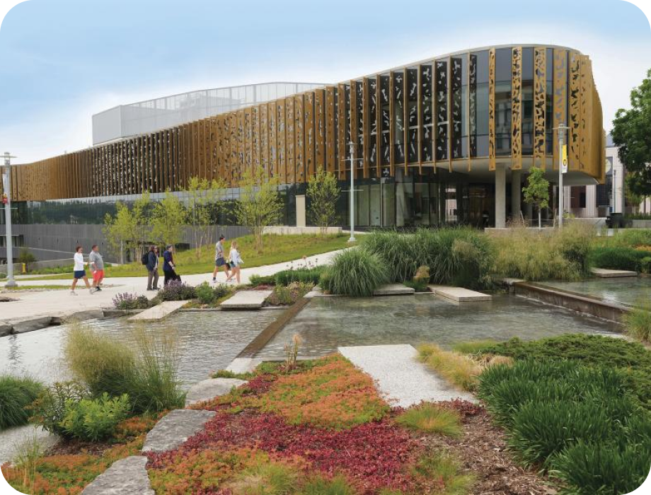 Modern building with landscaped gardens and pathways, people walking around.