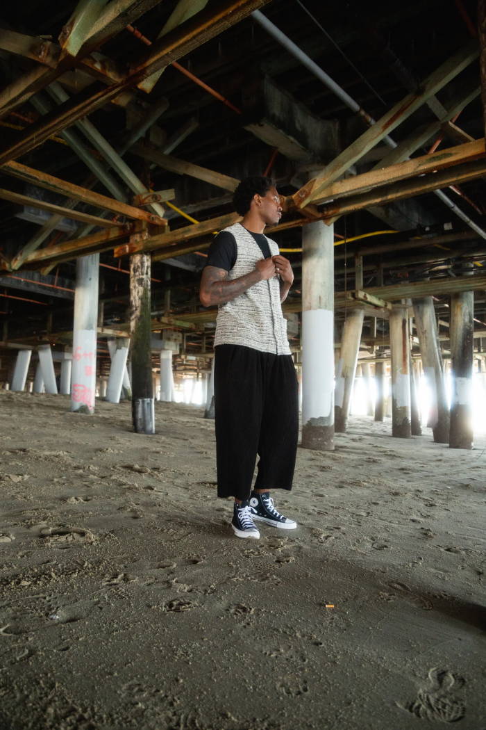 male model standing under pier with black converse on