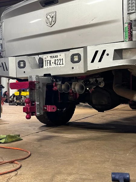 Rear view of silver Ram 2500 with train horns, pink drop hitch, and aftermarket bumper in garage