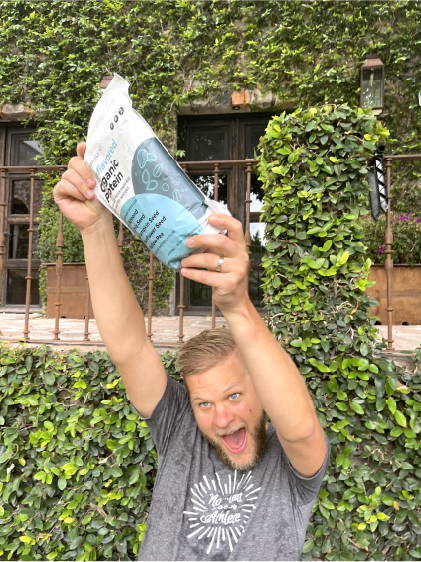 Complement vegan ambassador Doug Hay is holding up a pouch of Complement Protein with lots of excitement. 