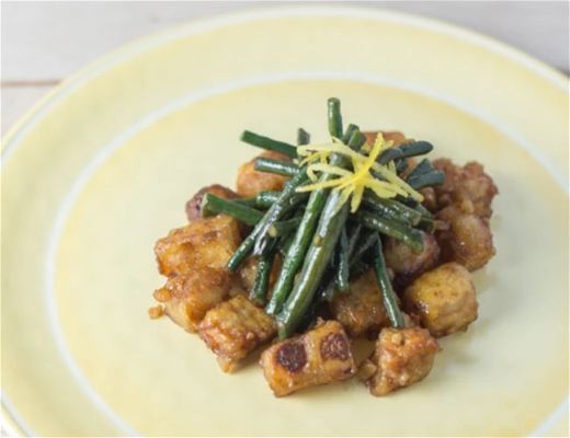 Plate of fried tofu with green beans and lemon zest garnish.