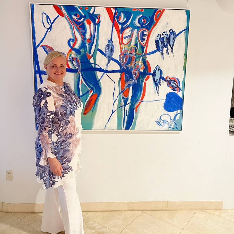 Camilla Webster wearing blue coral printed silk top woth white pants at a gallery with her paintings by Ala von Auersperg