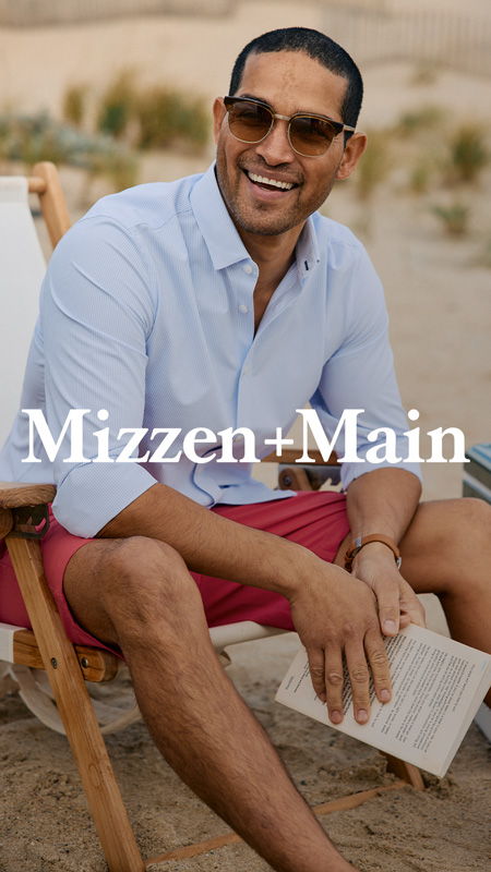 Man sitting on the beach, wearing sunglasses and a light blue shirt.