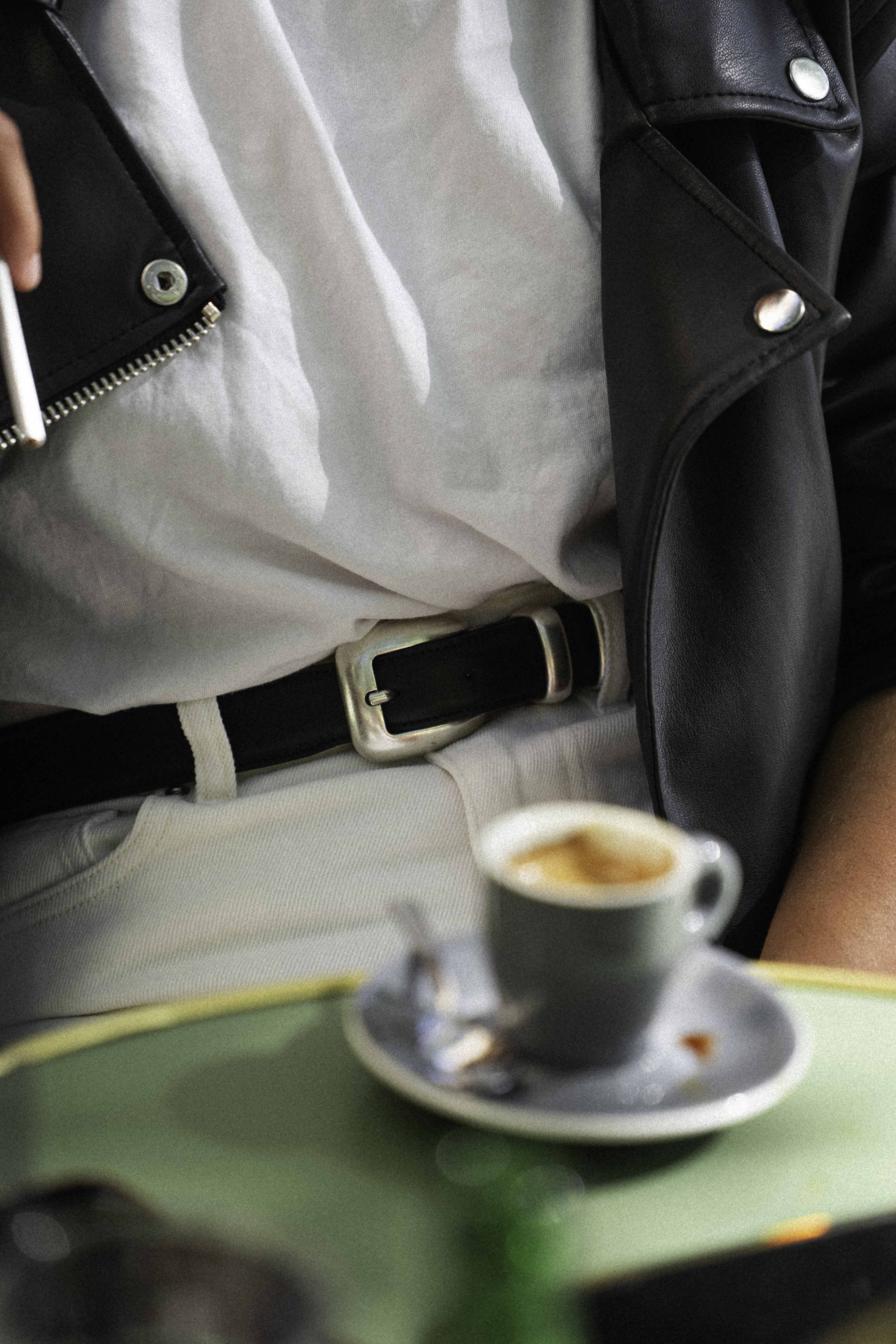 A person holding a cigarette beside a small cup of espresso.
