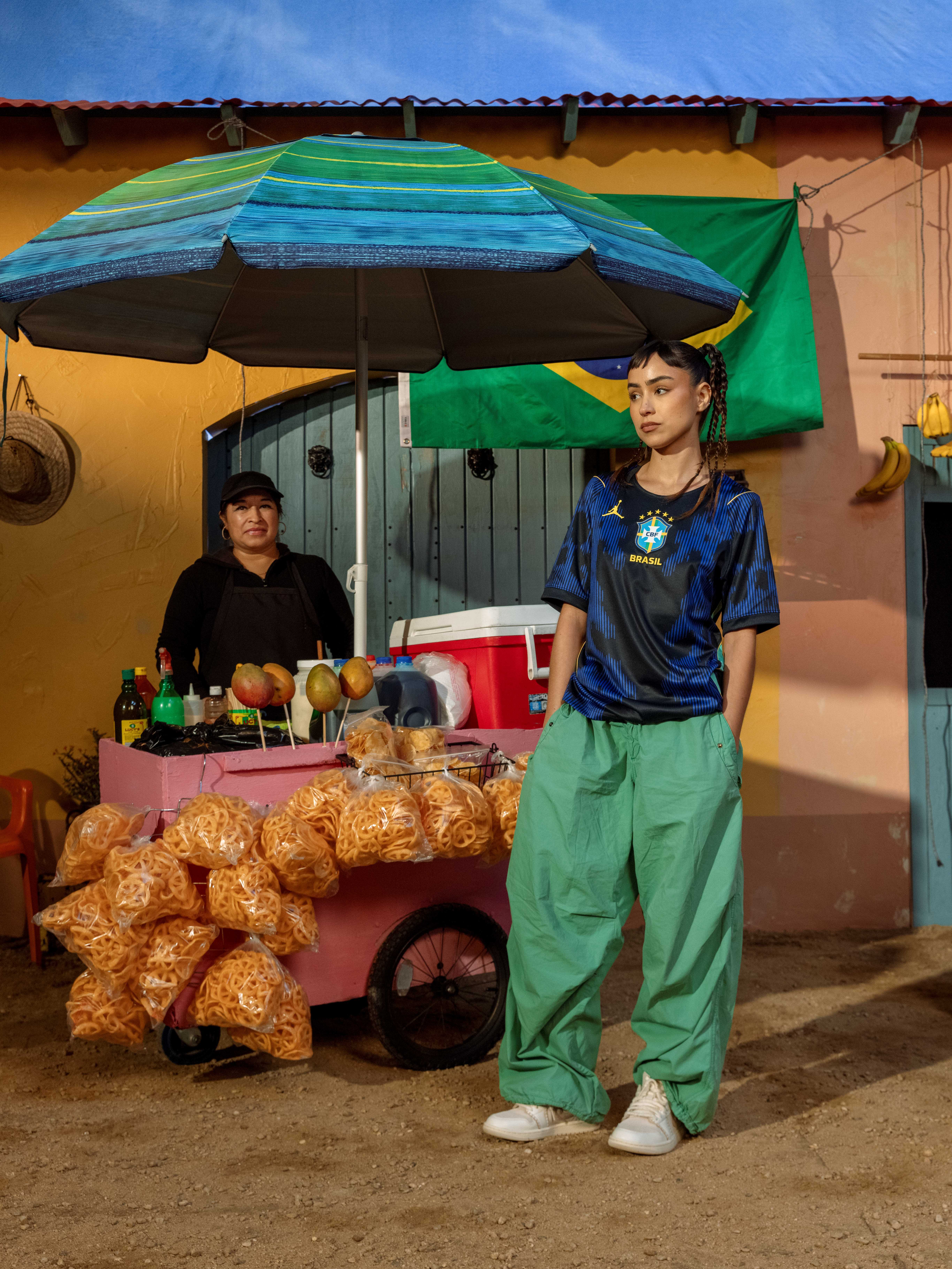 Person standing next to a food cart under an umbrella, with another person behind.