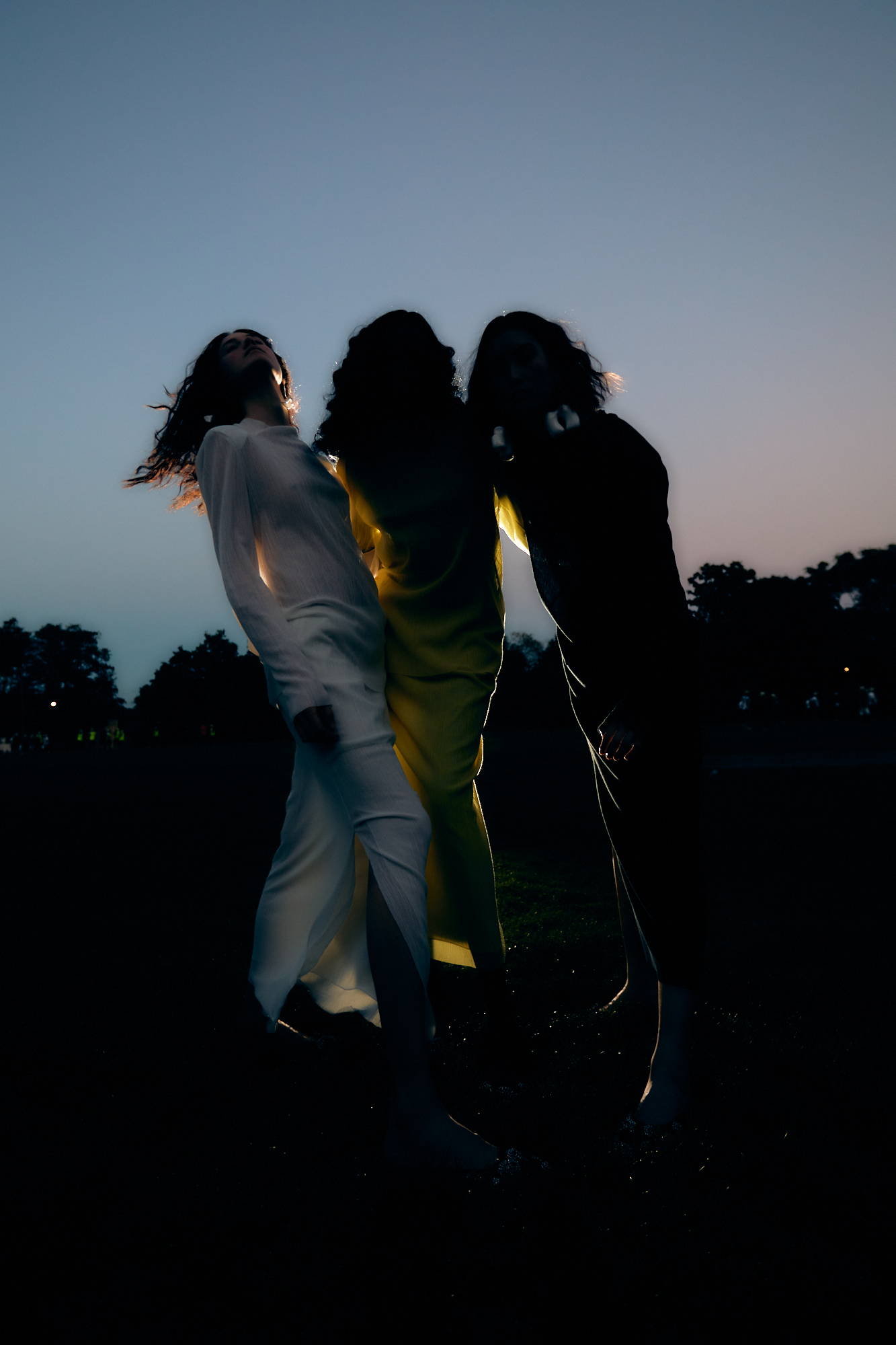 Three figures in flowing garments at dusk, illuminated by soft light.