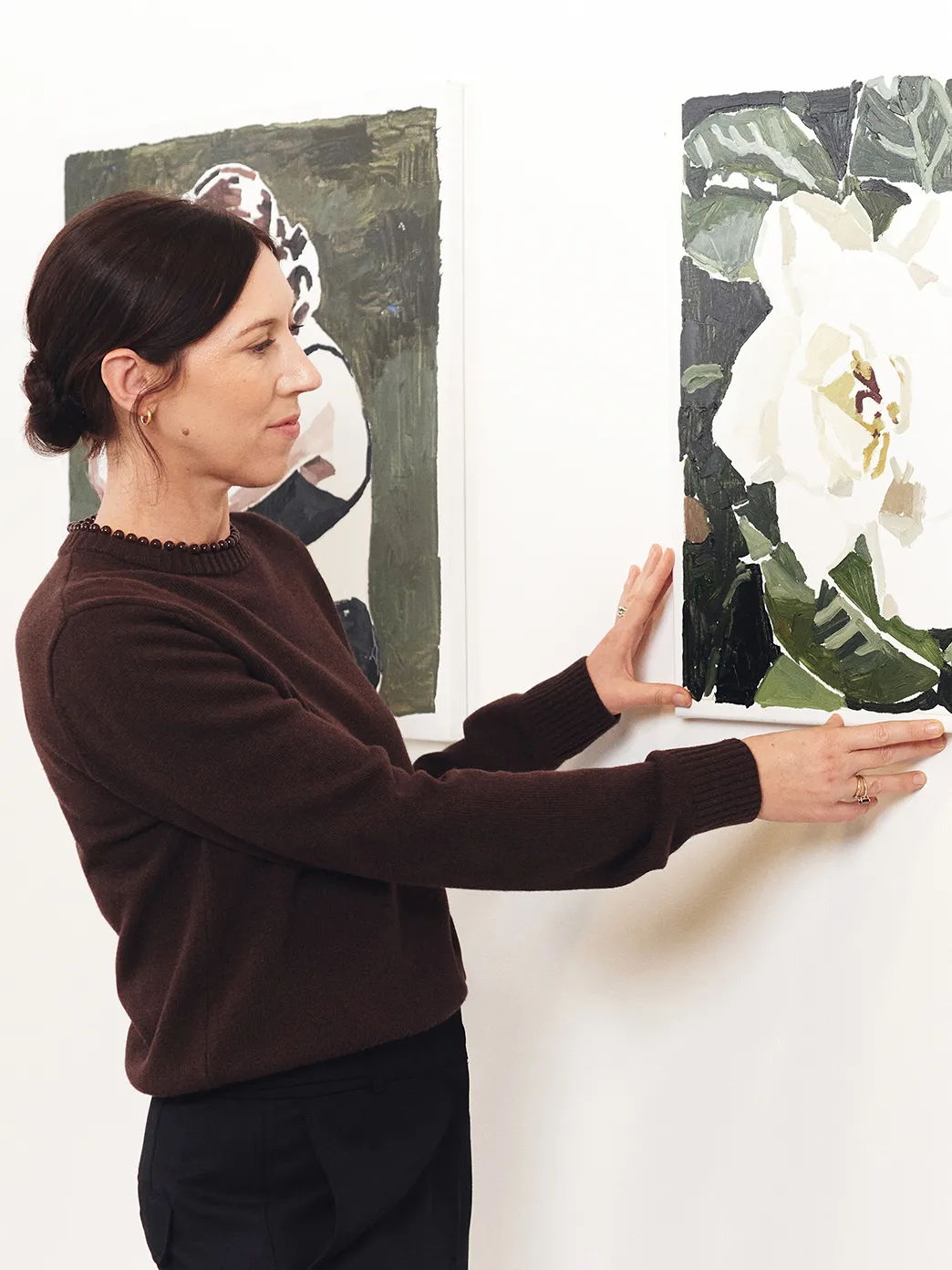 Person adjusting artwork on a wall, showcasing two different paintings.