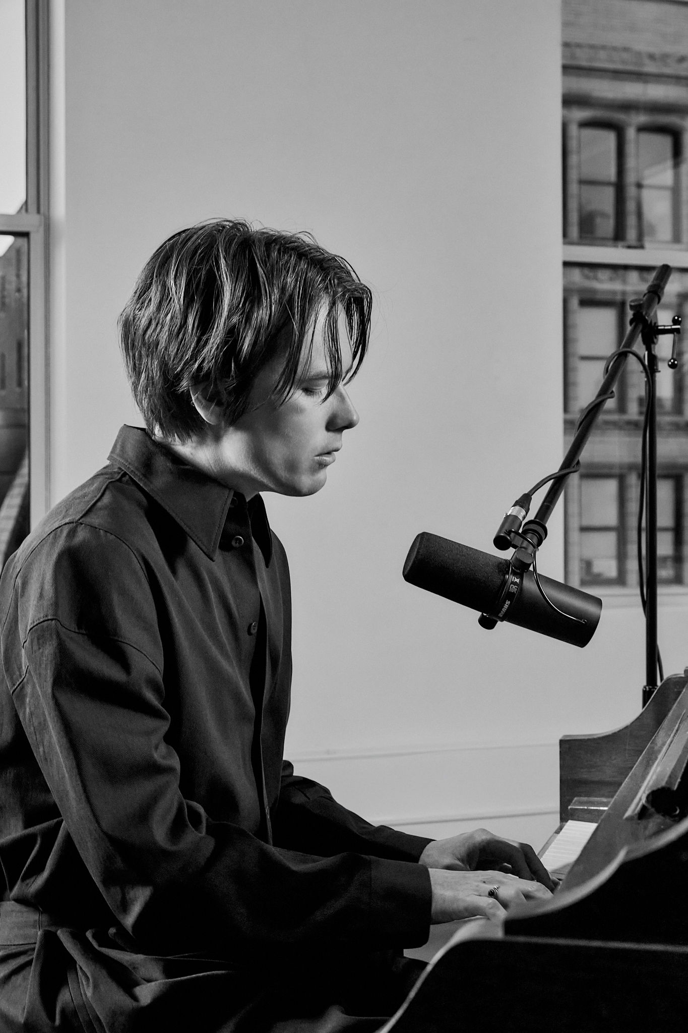 Person playing piano with microphone in a black and white setting.