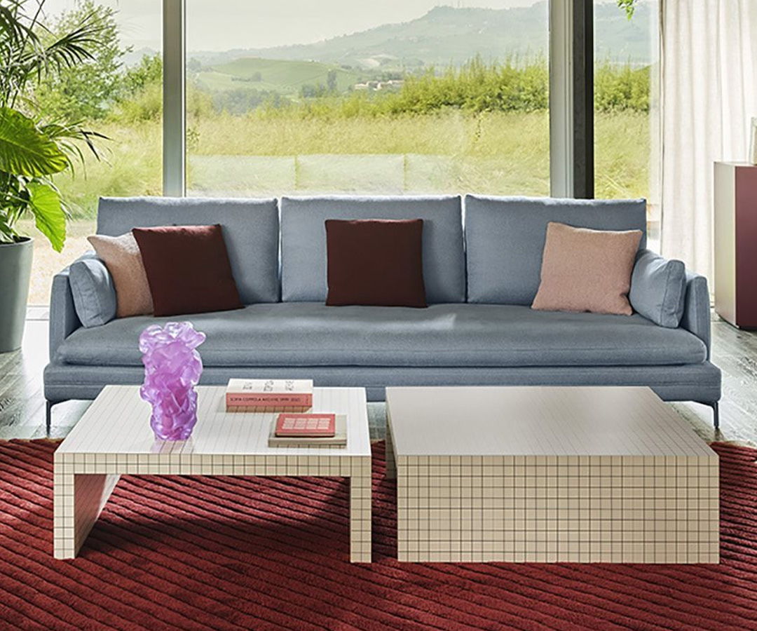 Living room with a blue Zanotta sofa, coffee tables, and a view of nature.
