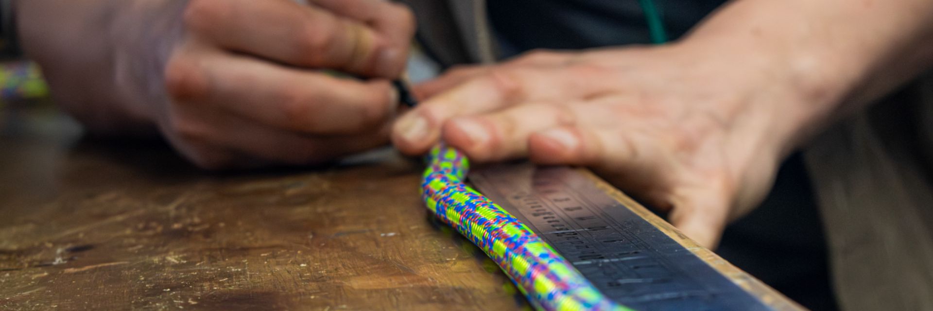 A person marking a colorful rope on a wooden surface.