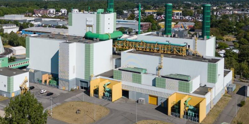 Industrial facility with green and yellow structures, surrounded by urban landscape.