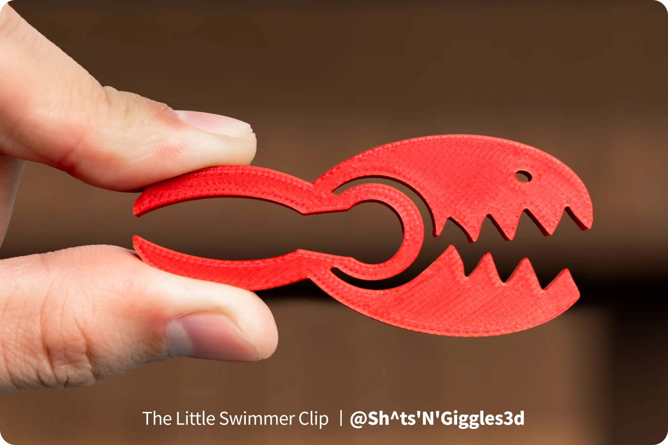 Red lobster-shaped clip held between fingers against a blurred background.