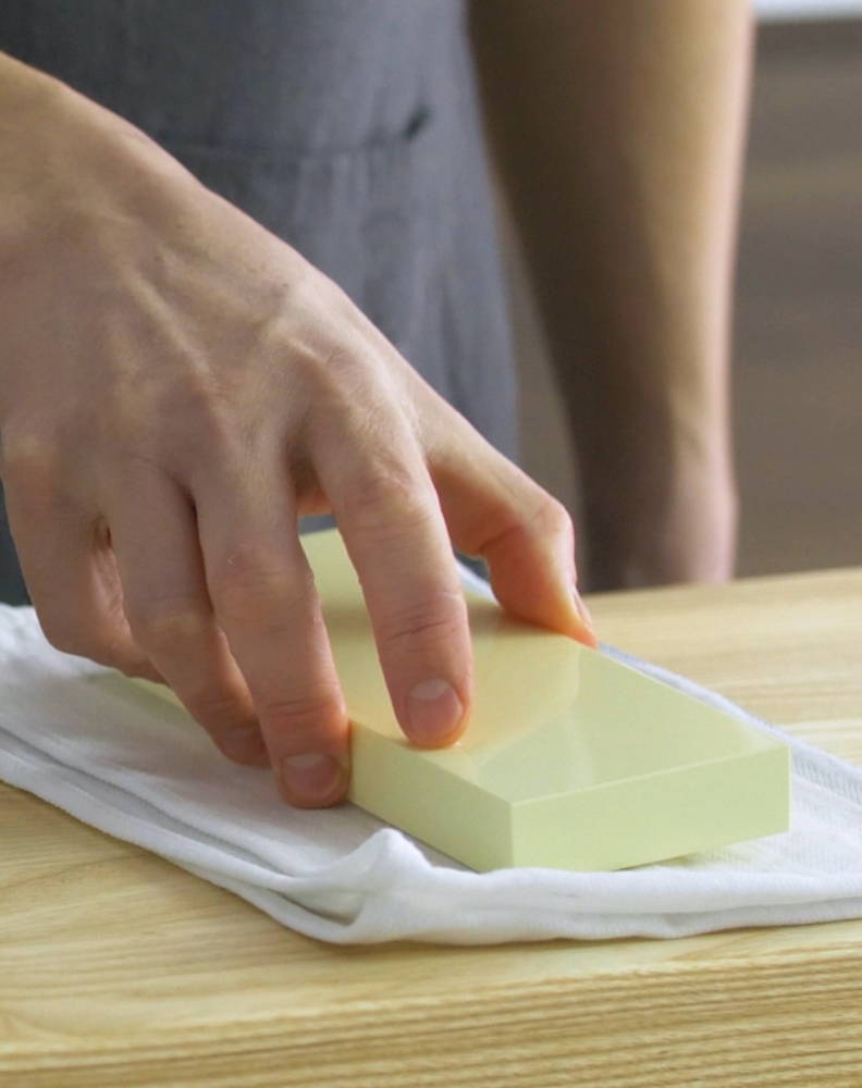 A chef placing a wet 6000-grit Misen Sharpening stone onto a kitchen towel on a wood countertop.