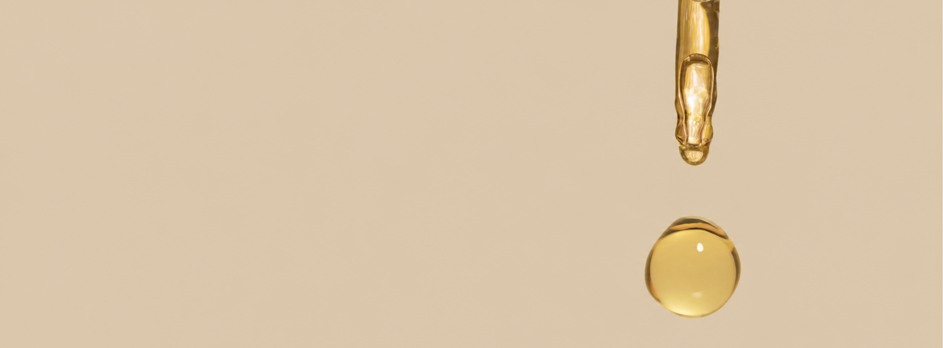 A drop of golden oil suspended above a beige background.
