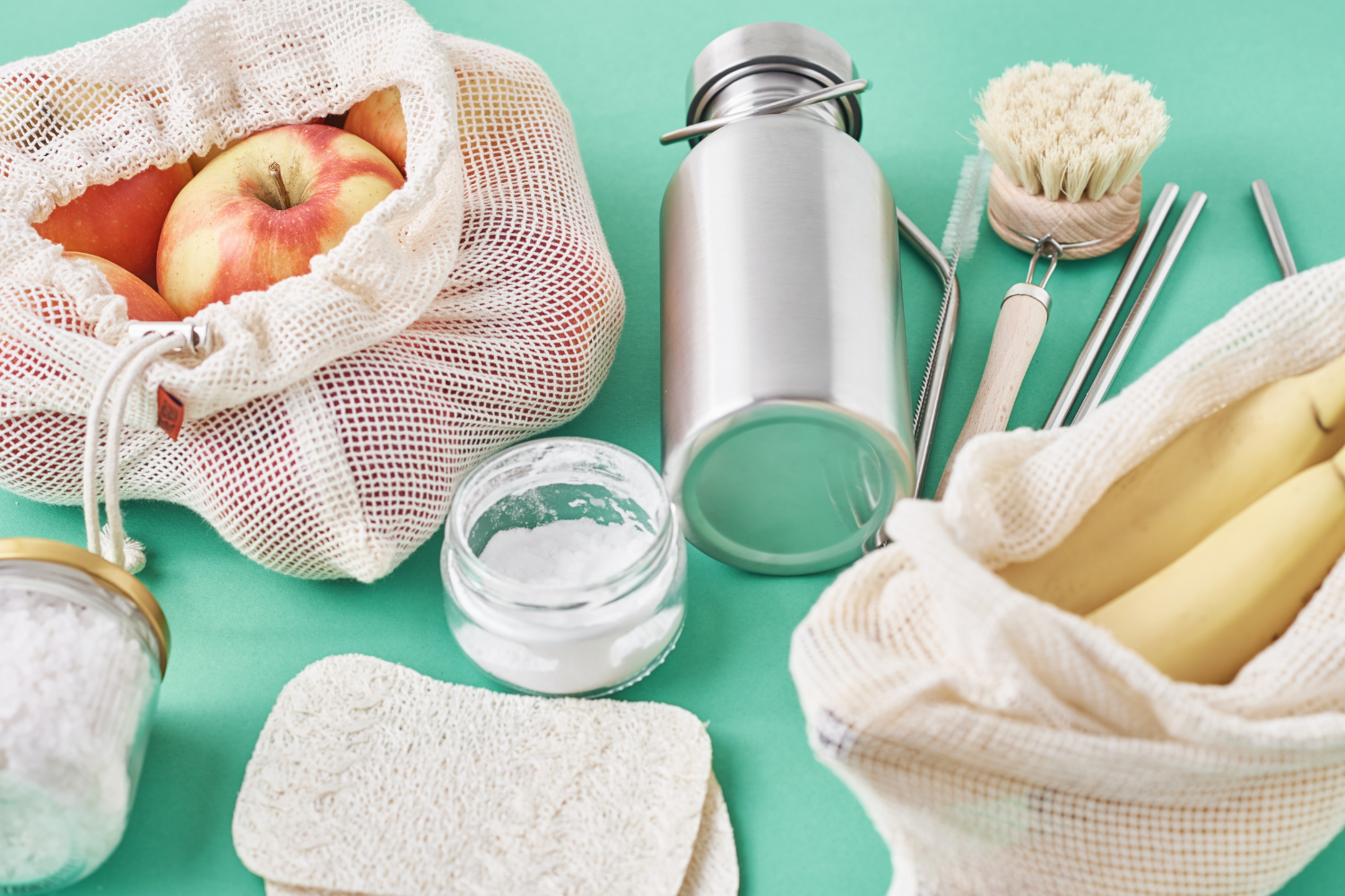 Reusable bags and containers with fruits and eco-friendly items on a green background.